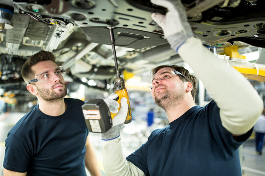 Two colleagues working at car underbody in modern factory