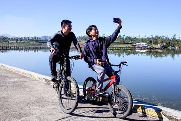 Fototapeta premium Cyclists Taking Break To Snap Selfie And Rest Beside Tranquil Lake