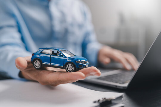 Car insurance and loan approval concept. A miniature car placed on hand with insurance contract document policy agreement. vehicle finance, policy management, rental, sales, and claims service.