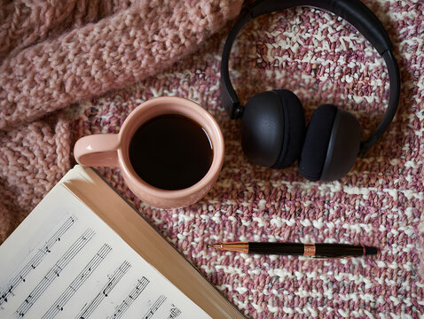 Cozy desk flat lay book headphones coffee cup music score pen on knitted blanket evoking relaxed creative morning