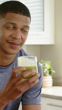 Vertical video: Clinking glasses, man in blue tee sipping green drink in kitchen, copy space