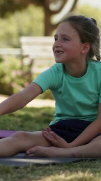 Vertical video: Reaching child on mat hearing off-frame call, extending right arm in park, mint tee
