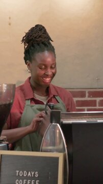 Vertical video: Barista in green apron making espresso, grinder at counter as customer approaching