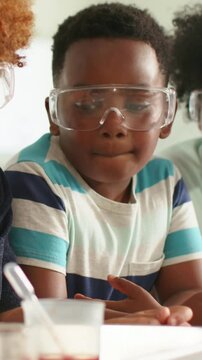Vertical video: Zooming in redhead holding dish as peers using pipette testing at school, goggles