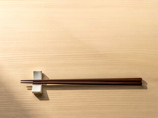 明るい木目調のテーブルに置かれた木製の箸と白い箸置き。日本の食文化やおもてなし、ミニマルな和の美学を表現した清潔感のあるダイニング風景。