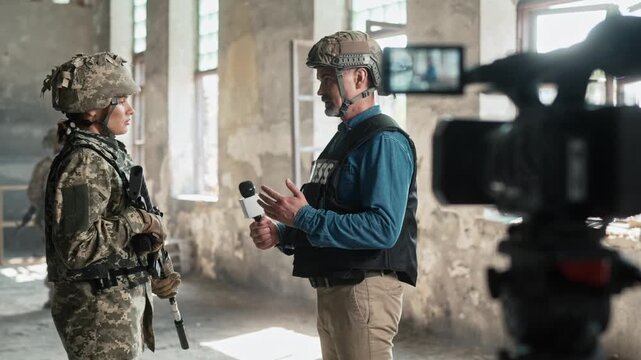 Military reporter taking interview of brave female soldier. Fearless man with microphone asking questions of armed woman with weapons. People in bulletproof vests and helmets talking to camera.
