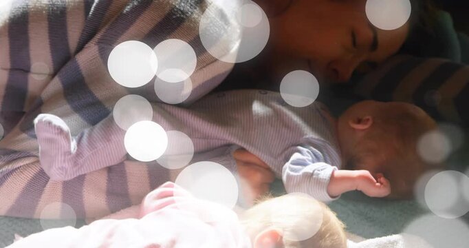 Mother resting with two infants on blanket, moving bokeh overlay, rising light revealing parenting