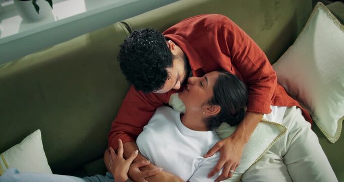 Couple, relax and laugh on sofa with kiss, romantic connection or bonding together on weekend break. Above, happy people and cuddle in home with support, affection or commitment for healthy marriage.