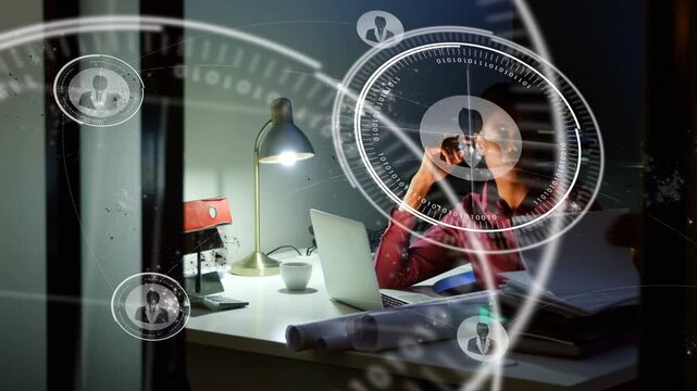 Woman working late, reviewing project plans on laptop and starting HUD overlays across glass door
