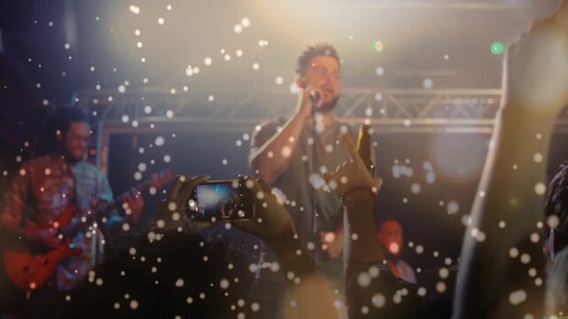 Lead singer starting song, concert band playing while confetti falling and phones capturing show