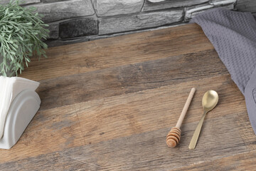 Wooden table with honey dipper and gold spoon next to napkin and plant in kitchen setting