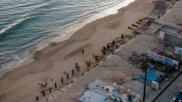 Aerial view of the meeting point between the ocean and the sandy beach, where remnants of structures stand, Malibu, California, United States.