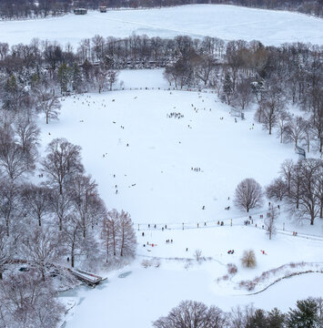 Aerial view of a snow-covered Central Park's landscape, where tiny figures skate across the frozen lake, contrasted by the dark silhouettes of bare trees, Manhattan, New York, United States.