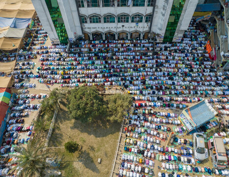 Aerial view of worshippers gathered shoulder-to-shoulder in prayer, their white caps a stark contrast to the mosque's facade, Charmonai, Barisal Division, Bangladesh.