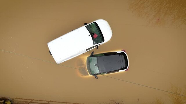 Flooded cars after heavy rainstorm covering road with deep muddy water. Extreme weather conditions leaving vehicles partially submerged in rural flood zone. Severe storm damage causing traffic