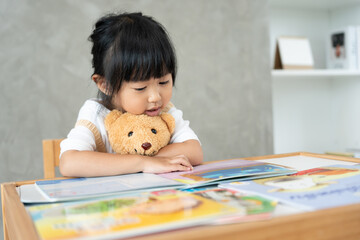 Naklejka premium Happy Asian children relax read book at home. daughter and reading a story. learn development, childcare, laughing, education, storytelling, practice, imagine, reduce addiction mobile phone