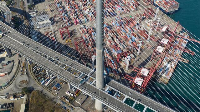 New Territories, Hong Kong - 15 February 2026: Aerial view of the colossal Stonecutters Bridge soaring above a bustling port with stacked containers in a symphony of red, blue, and yellow hues.