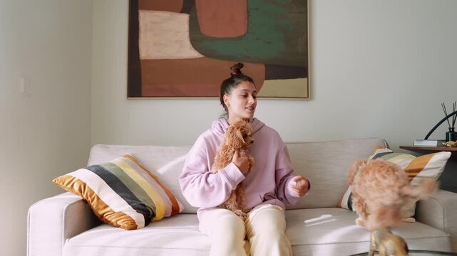 Woman gently holds her puppy on couch during sunny morning in stylish room