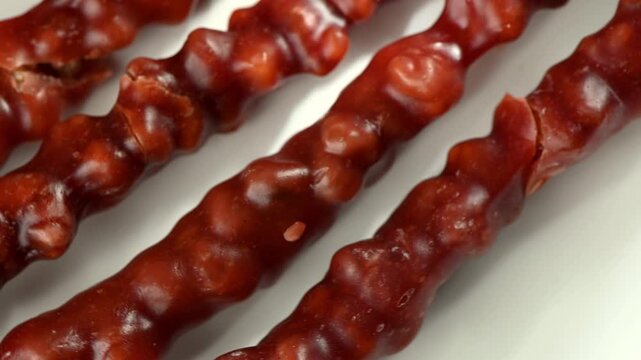 Macro close up of Churchkhela, a traditional Georgian candy filled with whole walnuts, slowly rotating on a turntable. Rich grape syrup coating, glossy surface, and detailed nut texture captured in hi