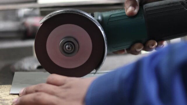 Close up of a worker cutting a metal plate using an electric angle grinder in a workshop with bright orange sparks flying from the rotating abrasive disc during the industrial fabrication process.