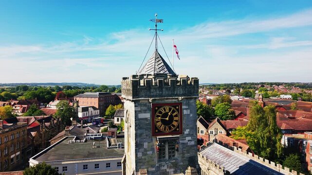 Cinematic drone aerial of the historic clock tower of St Thomas's Church in Salisbury Wiltshire England with surrounding town rooftops and countryside under blue sky.