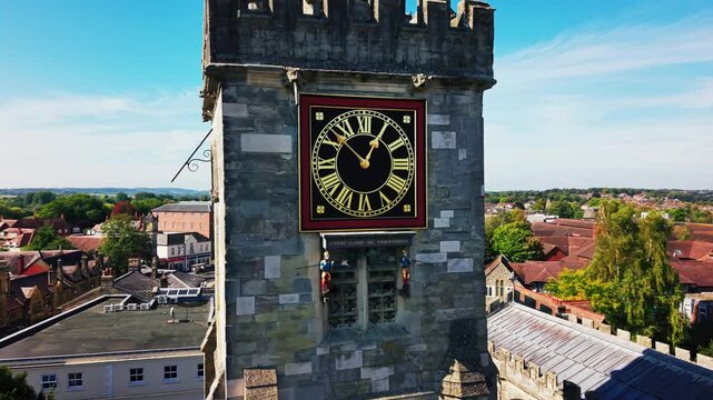 Close aerial drone shot of the historic clock tower of St Thomas's Church in Salisbury Wiltshire England with town rooftops and countryside in the background.