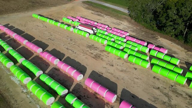 Cotton module transport truck positioned among parallel rows of wrapped cotton bales on farmland near Headland, Henry County, Alabama, United States during harvest operations, aerial view.