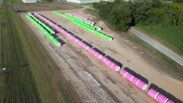 Parallel rows of wrapped cotton bales resting on farmland near Headland, Henry County, Alabama, United States during autumn harvest season, static aerial view.