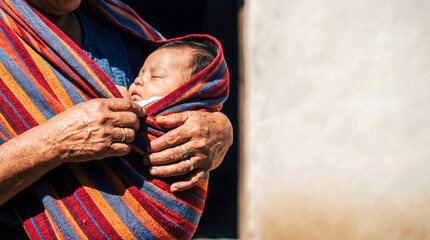 Mexican mother wrapping baby bright striped rebozo copy space mexico traditional textile clothing culture parenting family care holding close up lifestyle