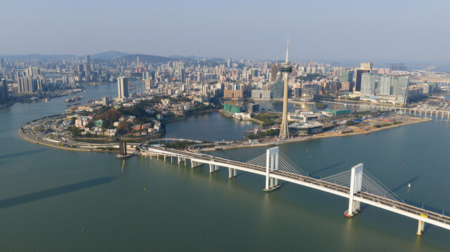 Aerial view of the iconic Macau Tower piercing the skyline amidst modern buildings and bridges reflecting the azure waters, Macau, Macao.
