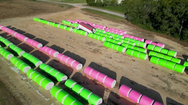 Plastic wrapped cotton modules arranged in long parallel rows across farmland near Headland in Henry County, Alabama within the Wiregrass agricultural region while transport truck collects bales