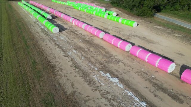 Plastic wrapped upland cotton (Gossypium hirsutum) modules organized in long parallel rows across agricultural land near Headland in Henry County, Alabama, aerial push in shot.