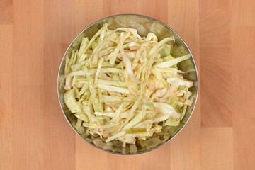 A top down view of a fresh shredded cabbage salad seasoned with spices in a round metal bowl on a...