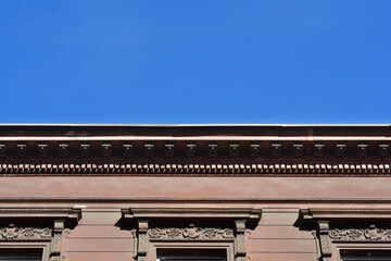 The upper part of a brown historic building facade features decorative window frames and an ornate cornice against a clear blue sky © nahhan