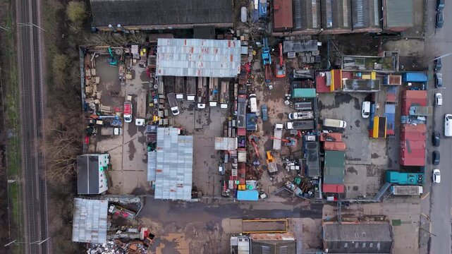Drone descent over scrapyard showing rows of scrapped cars, trucks, containers and workshops in an industrial breakers yard, aerial top-down view for recycling and demolition themes.