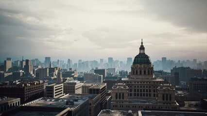 Obraz premium aerial skyline domed capitol cloudy sky, cinematic drone pan across historic dome, dense urban grid, highrise silhouettes fading into mist, muted tones
