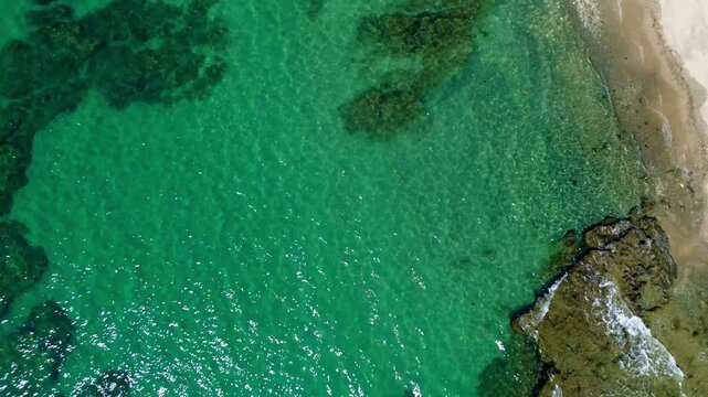 Winding up aerial drone view of the calm waves lapping at the shoreline with visible rocks and coral formation underneath the clear sea. Basay, Negros Oriental, Philippines
