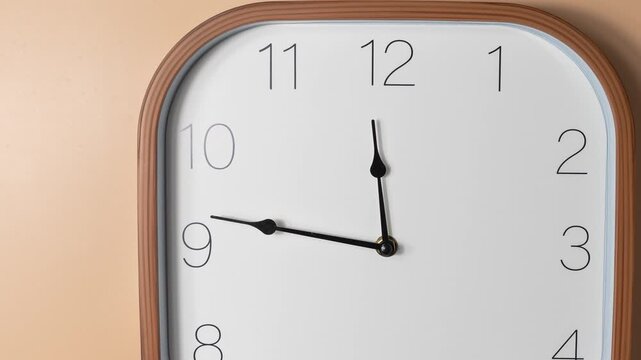 Close-up timelapse of a modern analog wall clock. The camera slowly pans from left to right across the dial as the clock hands move, emphasizing time passing in a clean minimal setting.