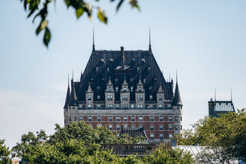 Quebec City, Canada - August 23, 2025: Fairmont Le Chateau Frontenac historic castle-style hotel with steep dark roof and turrets rising above green trees on a clear summer day © Andrei Antipov