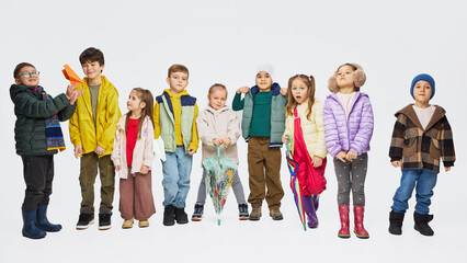 Fototapeta premium Group of children wearing colorful autumn outfits standing together in studio. Concept of kids fashion collection, seasonal clothing styles, playful childhood and modern children apparel.