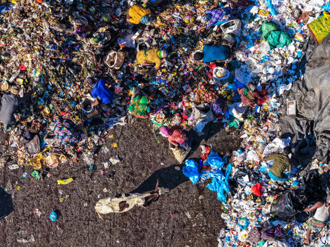 Chattogram, Bangladesh - 25 November 2025: Aerial view of a sprawling landfill where vibrant, colorful clothing contrasts with the dull, gray waste and dark shadows.