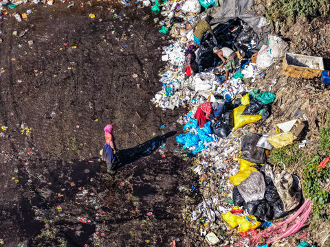 Chattogram, Bangladesh - 25 November 2025: Aerial view of vibrant colors of clothing cutting through the monochrome waste landscape at Anondobazar Landfill.