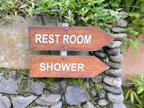 Wooden directional sign showing rest room and shower in tropical outdoor setting.
