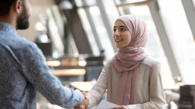 Business Handshake: A professional woman with headscarf, and a man are in a professional setting, a symbolic handshake sealing a new partnership. Capturing the essence of teamwork and agreement. 