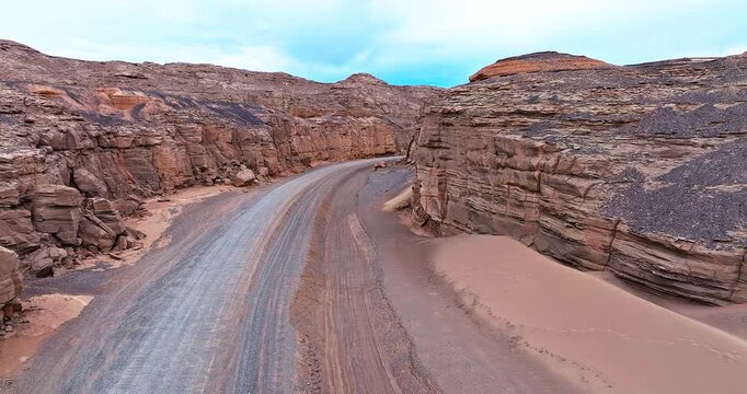 Aerial view of a winding gravel road through dramatic layered Yardang formations in the remote desert of Xinjiang, China.