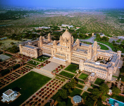 Aerial view of the majestic Umaid Bhawan Palace with its golden facade and meticulously designed gardens against a backdrop of arid landscape, Jodhpur, India.