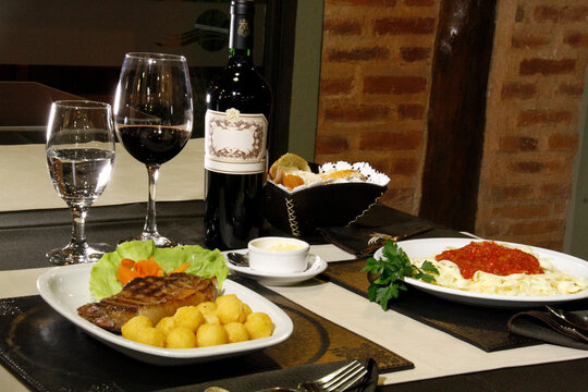 Cena gourmet con filete a la parrilla, pasta italiana y botella de vino tinto en mesa de restaurante