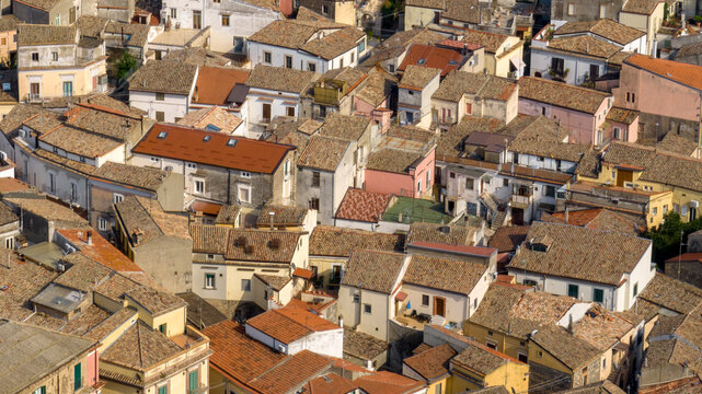 Aerial view of a Mediterranean village featuring a dense cluster of historic houses with traditional terracotta tiled roofs. It is the historic center of Melfi, a town in Basilicata, Southern Italy.