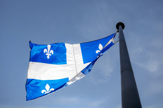 Quebec provincial flag with fleur-de-lis symbols flying on metal flagpole against clear blue sky seen from below