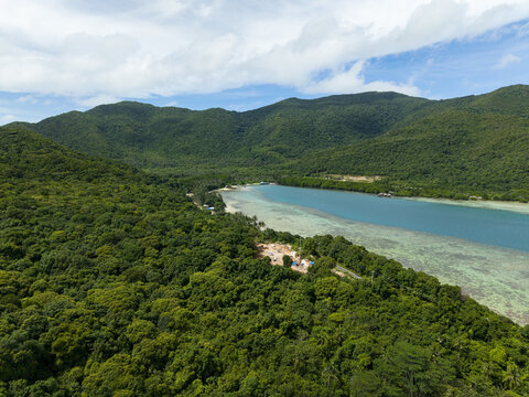 Aerial view of lush green forests meet the turquoise sea near Bobby Beach, a serene coastal landscape, Karimunjawa, Central Java, Indonesia.
